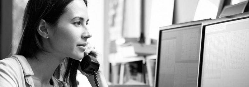 A woman on the phone while looking at her computer screens